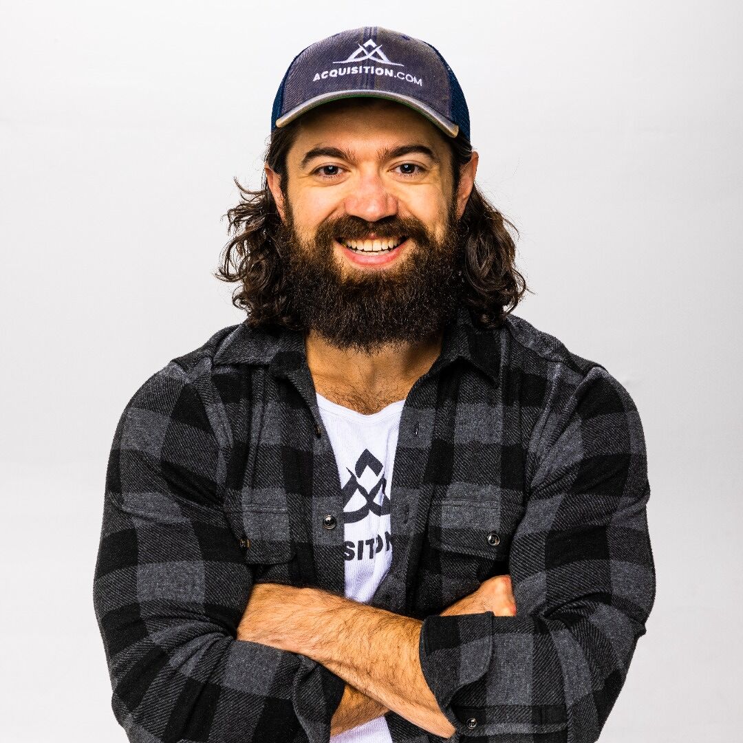 Portrait of Alex Hormozi in an Acquisition.com cap, arms folded.